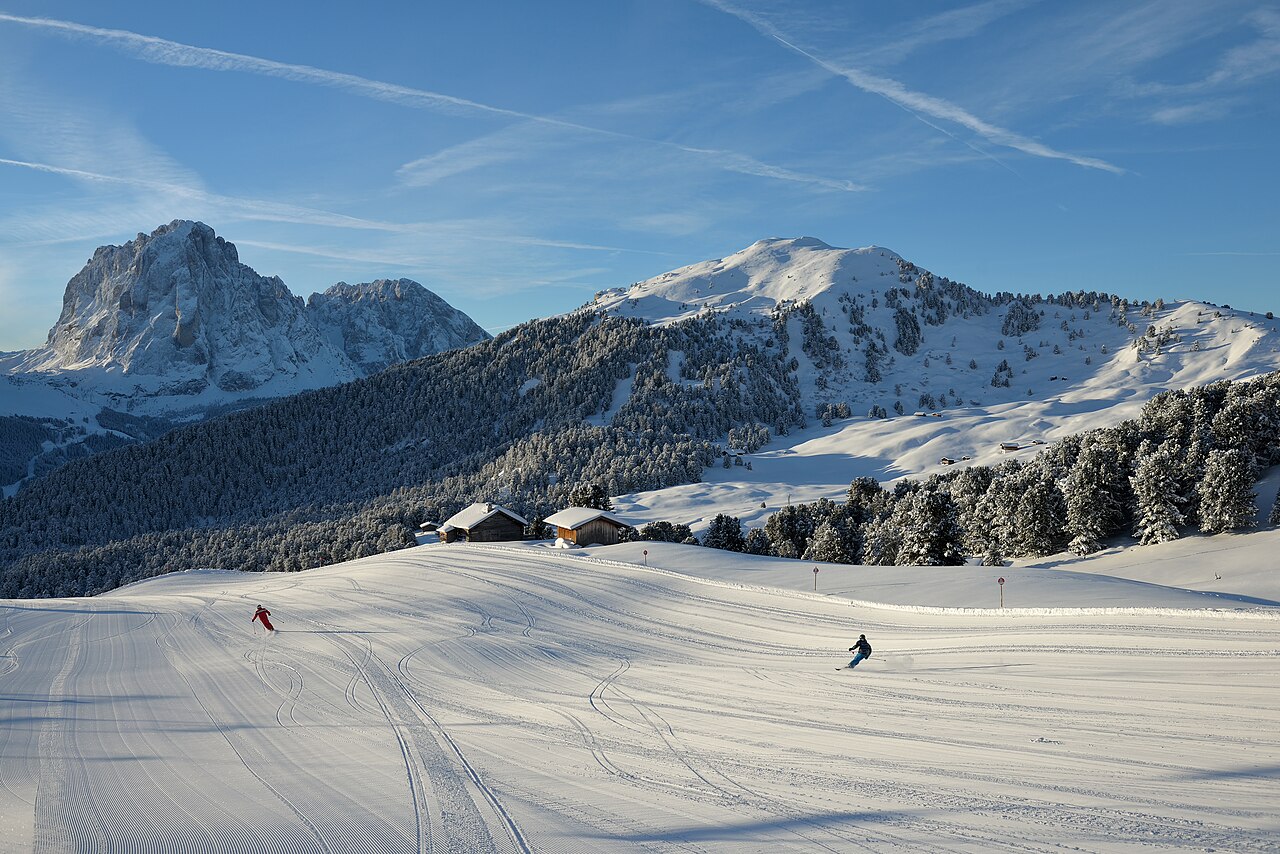 A wide groomed piste curving down an open snow slope below rocky peaks