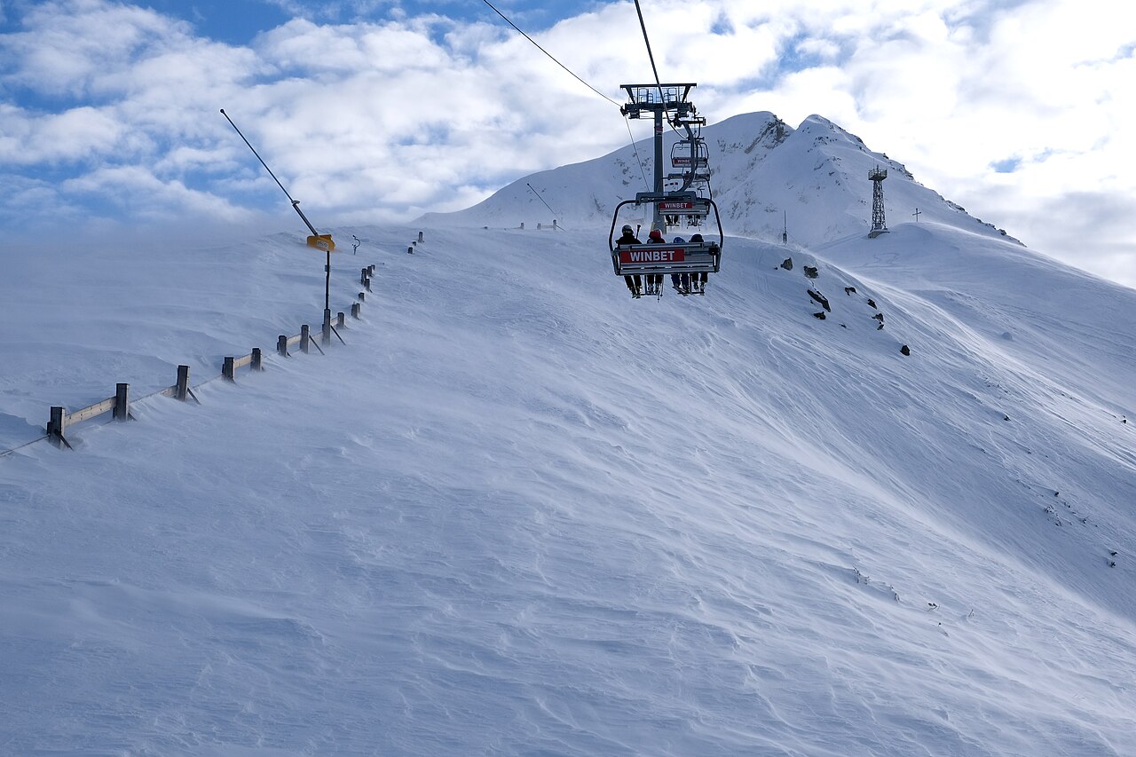 A chairlift carries skiers above wide snow-covered pistes lined with dark conifers