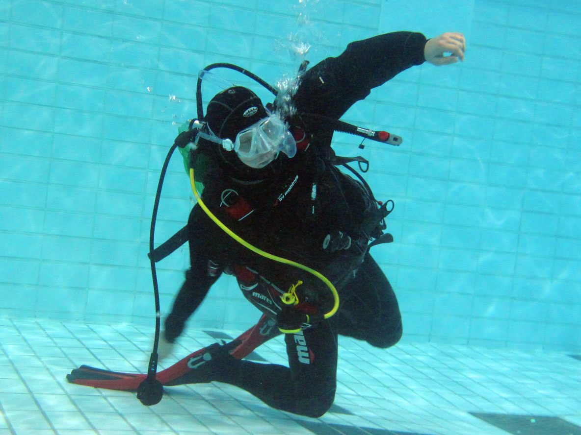 A scuba diver practicing regulator recovery underwater in a training pool