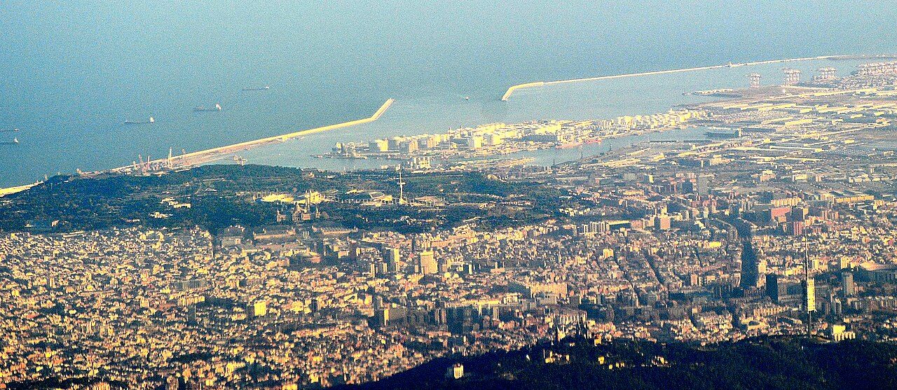 Aerial view of Barcelona and its Mediterranean coast, with the green hill of Montjuïc at left and the harbor beyond
