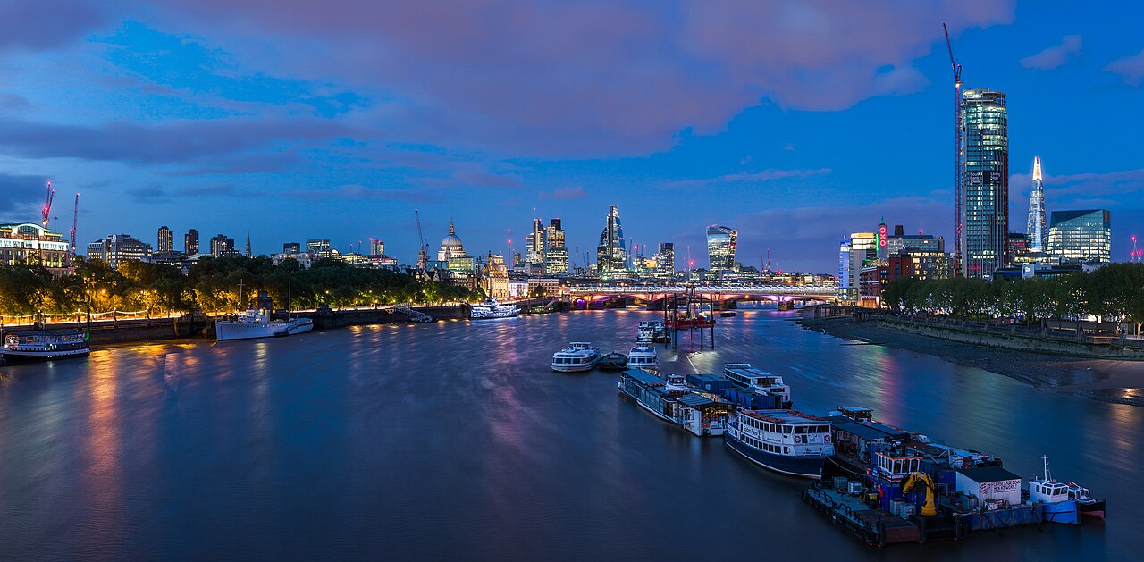 Boats on the Thames beneath the London skyline at blue hour, seen from Waterloo Bridge