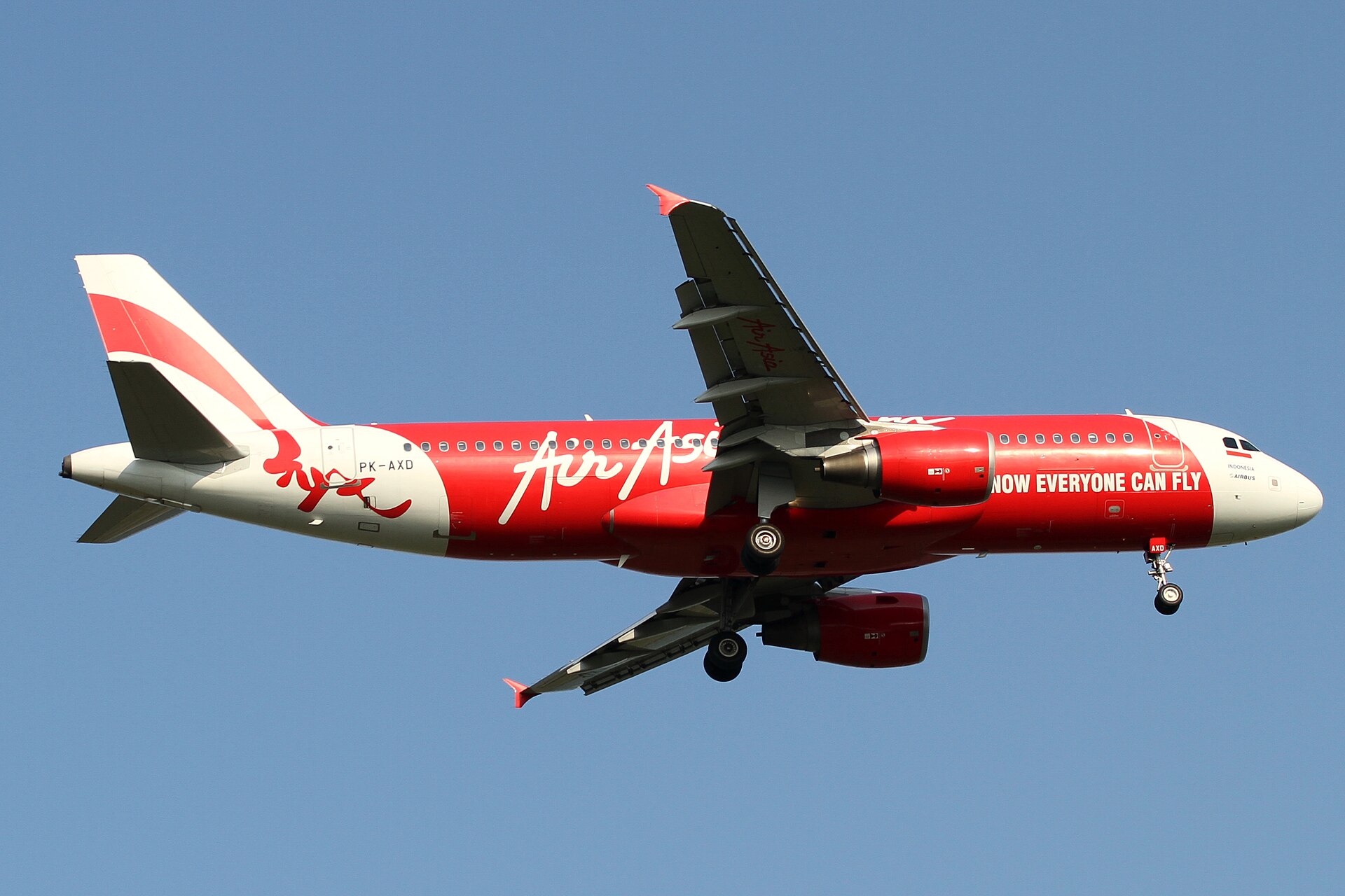 A red and white Indonesia AirAsia Airbus A320 on the taxiway with airport buildings behind it