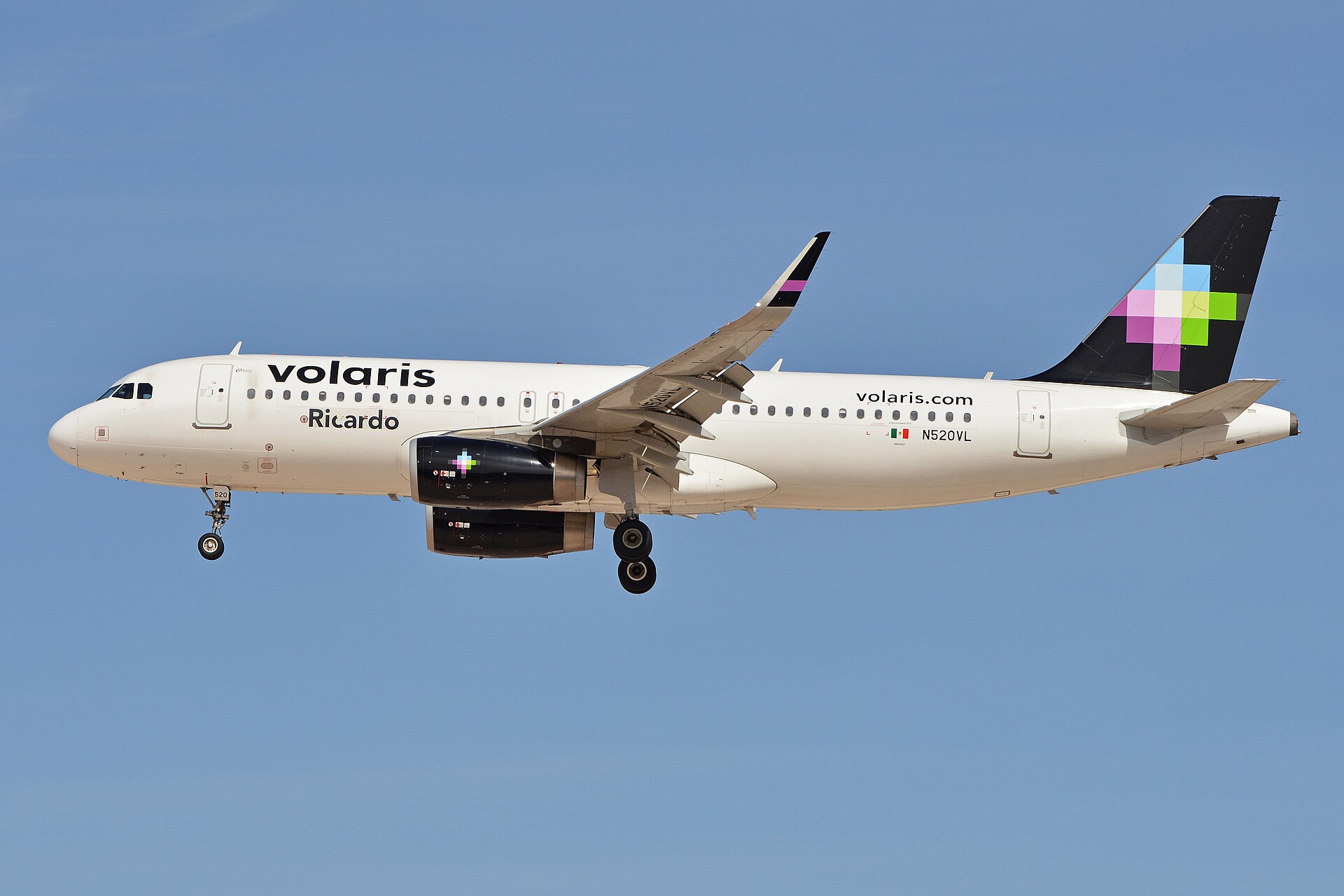 A white Volaris Airbus A320 with purple and orange tail markings on final approach with its landing gear down