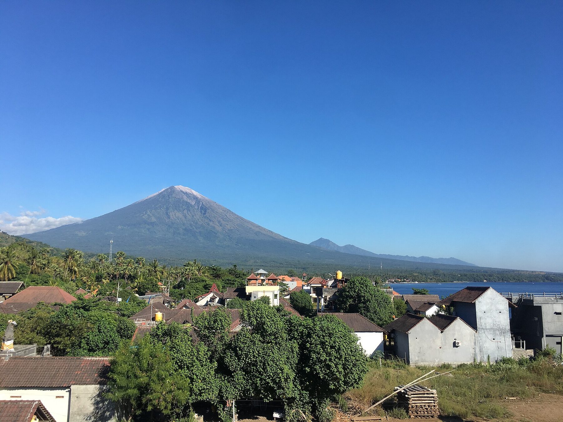 A dark volcanic coastline curving into the sea below the cone of Mount Agung, seen from Amed on Bali's east coast