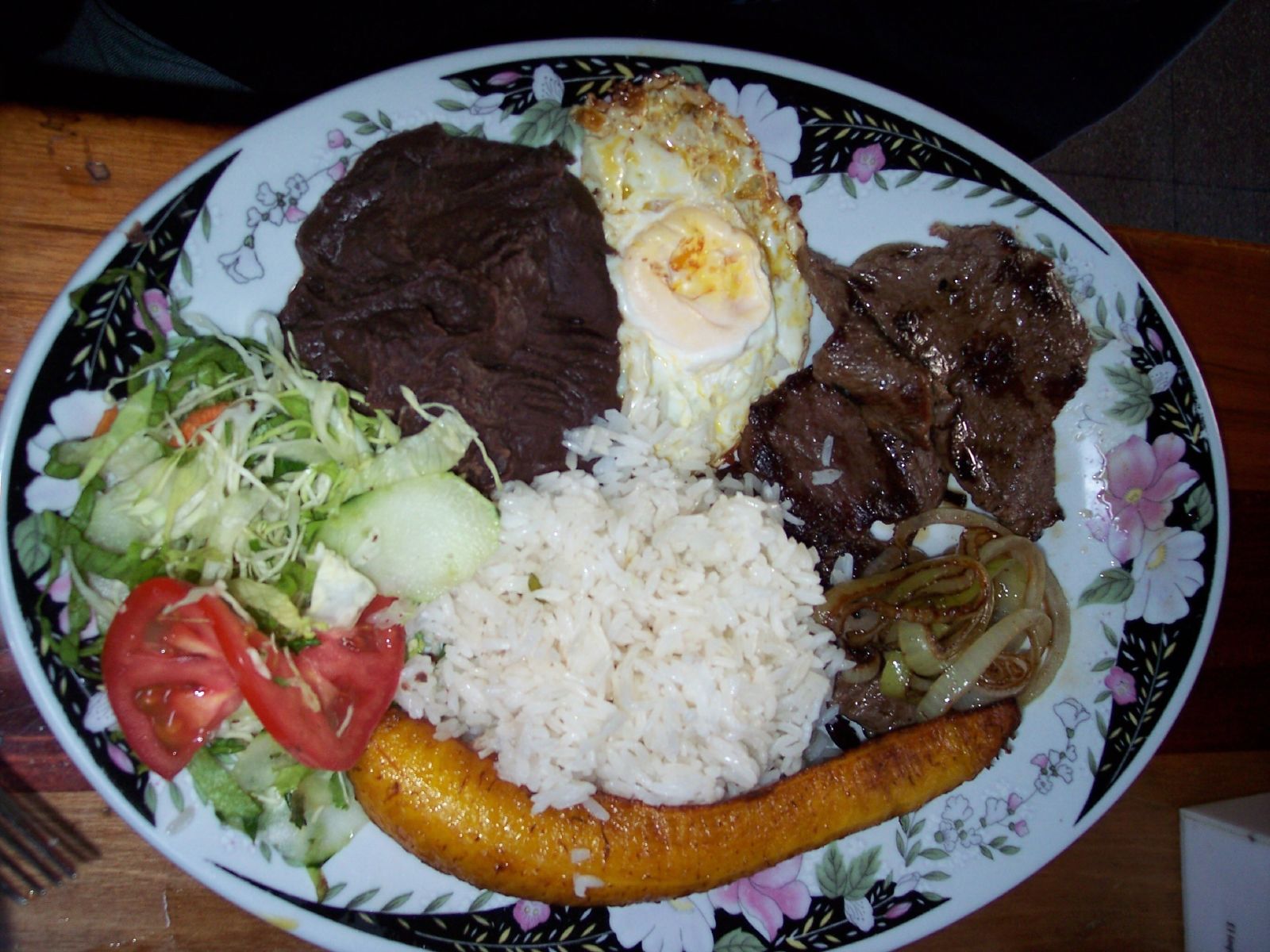 A plate of Costa Rican casado: white rice, black beans, fried plantain, a fried egg, shredded cabbage salad and meat cooked with onion
