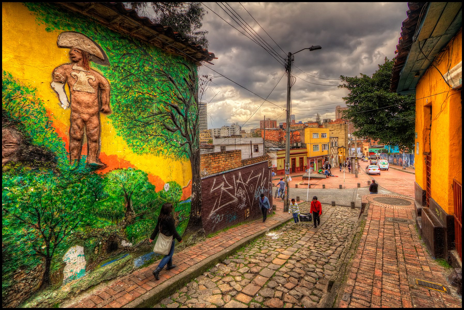 A narrow street of low colonial-era houses in La Candelaria, Bogotá, with painted facades and murals on the walls