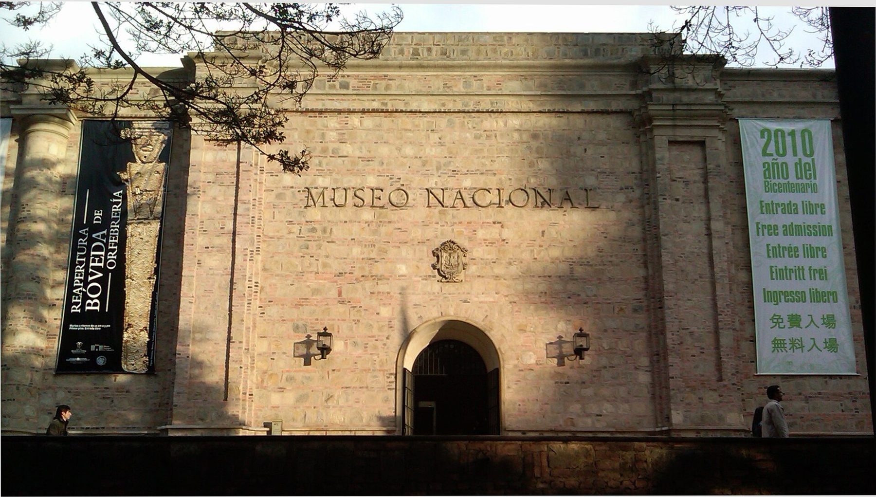 The stone front of the Museo Nacional de Colombia with the words Museo Nacional carved across it, an arched doorway below and a tall banner hanging at each side