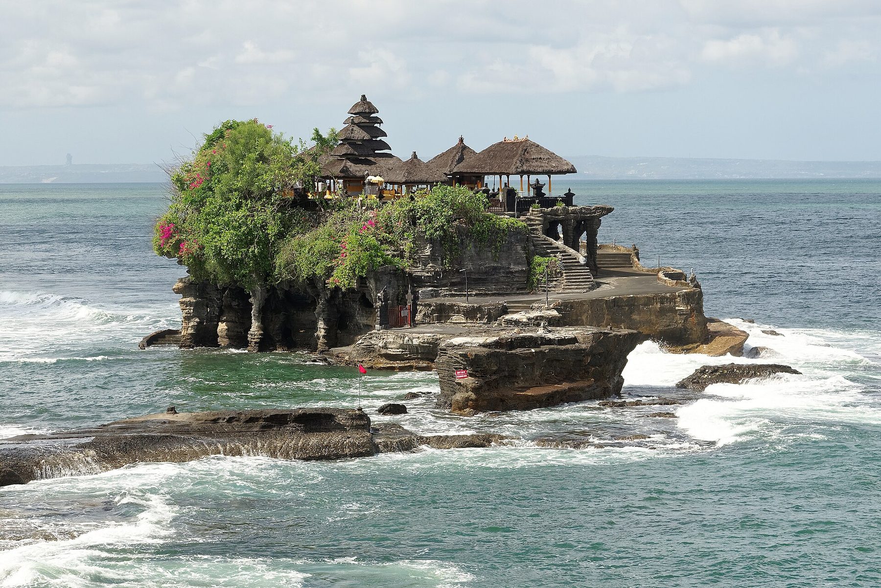 Pura Tanah Lot standing on its rock offshore at high tide, with waves breaking around the base
