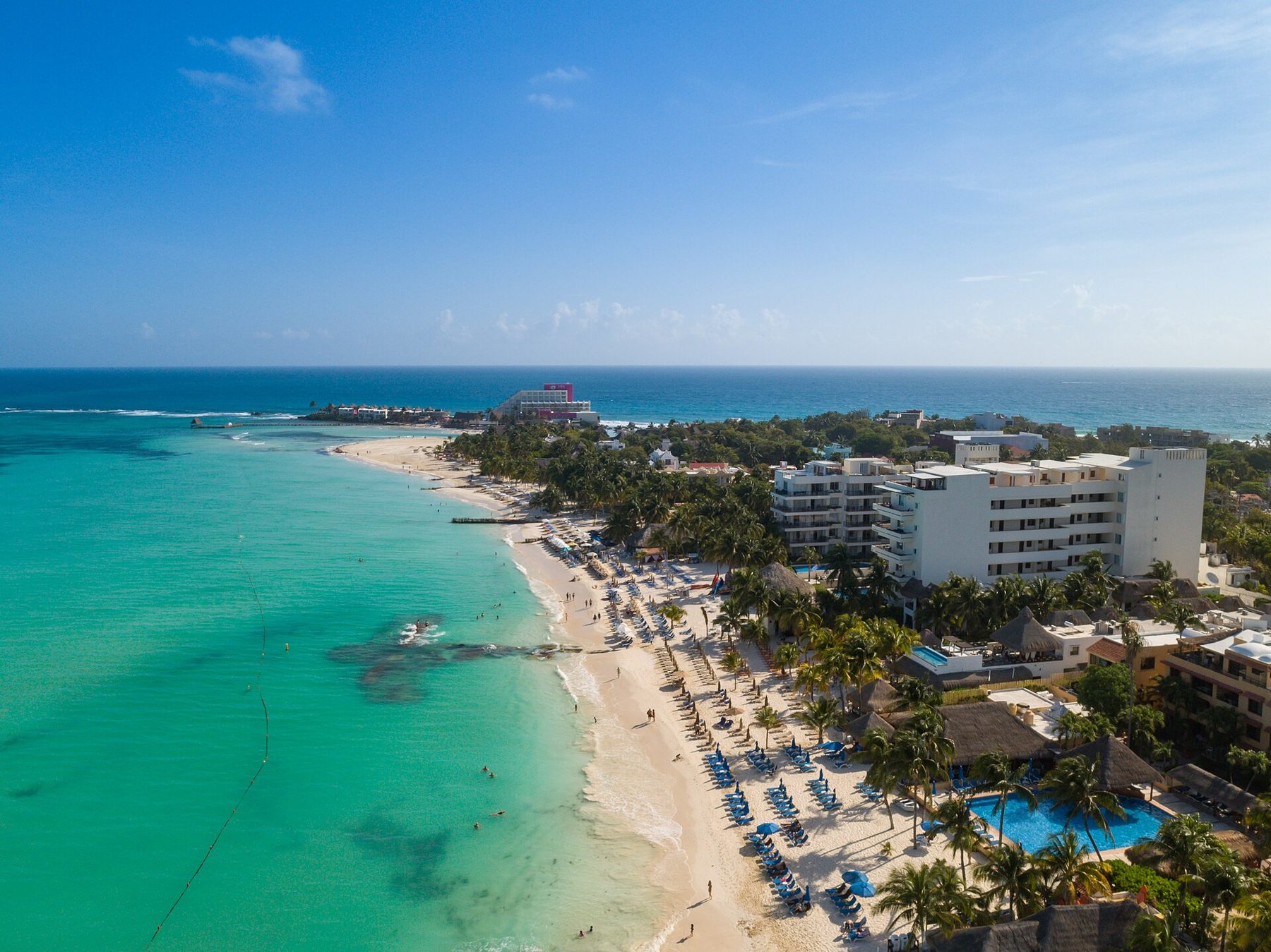 An aerial view of a white sand spit at Playa Norte on Isla Mujeres, with shallow turquoise water on both sides and small boats moored offshore