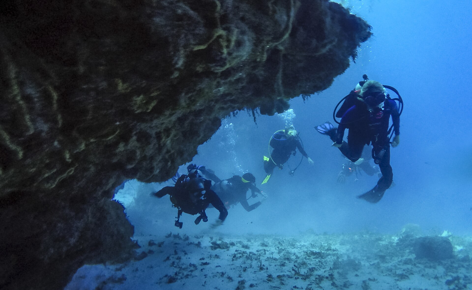 Two scuba divers pass through an arch in the coral, framed by reef above and below them, in blue water