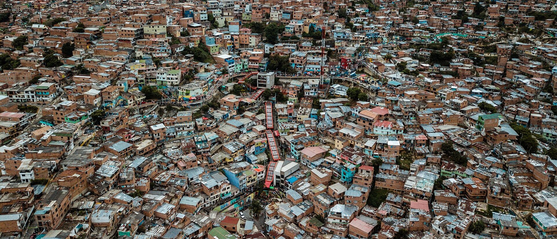 Covered outdoor escalators with orange roofs climb between brick and painted houses on a steep hillside