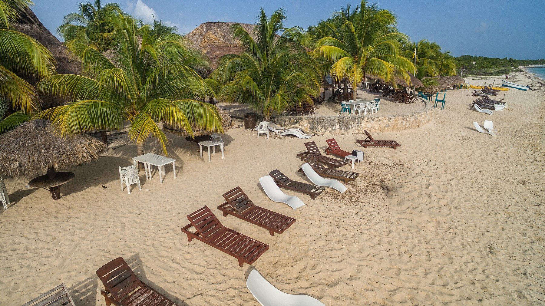 An aerial view of a curved white sand beach on Cozumel with palms behind it and pale reef water offshore