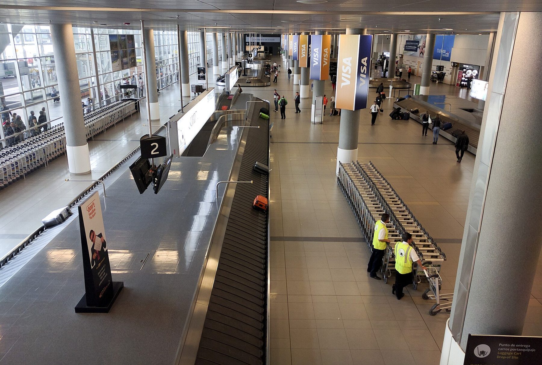 Travelers waiting around baggage carousels in a bright arrivals hall with a high white ceiling
