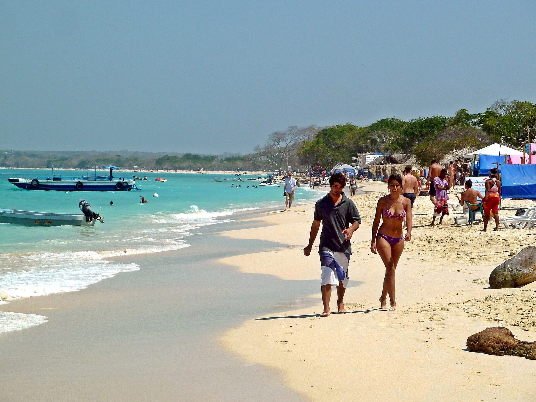 Pale sand and shallow turquoise water at Playa Blanca on Isla Barú, with thatched shade structures along the beach.