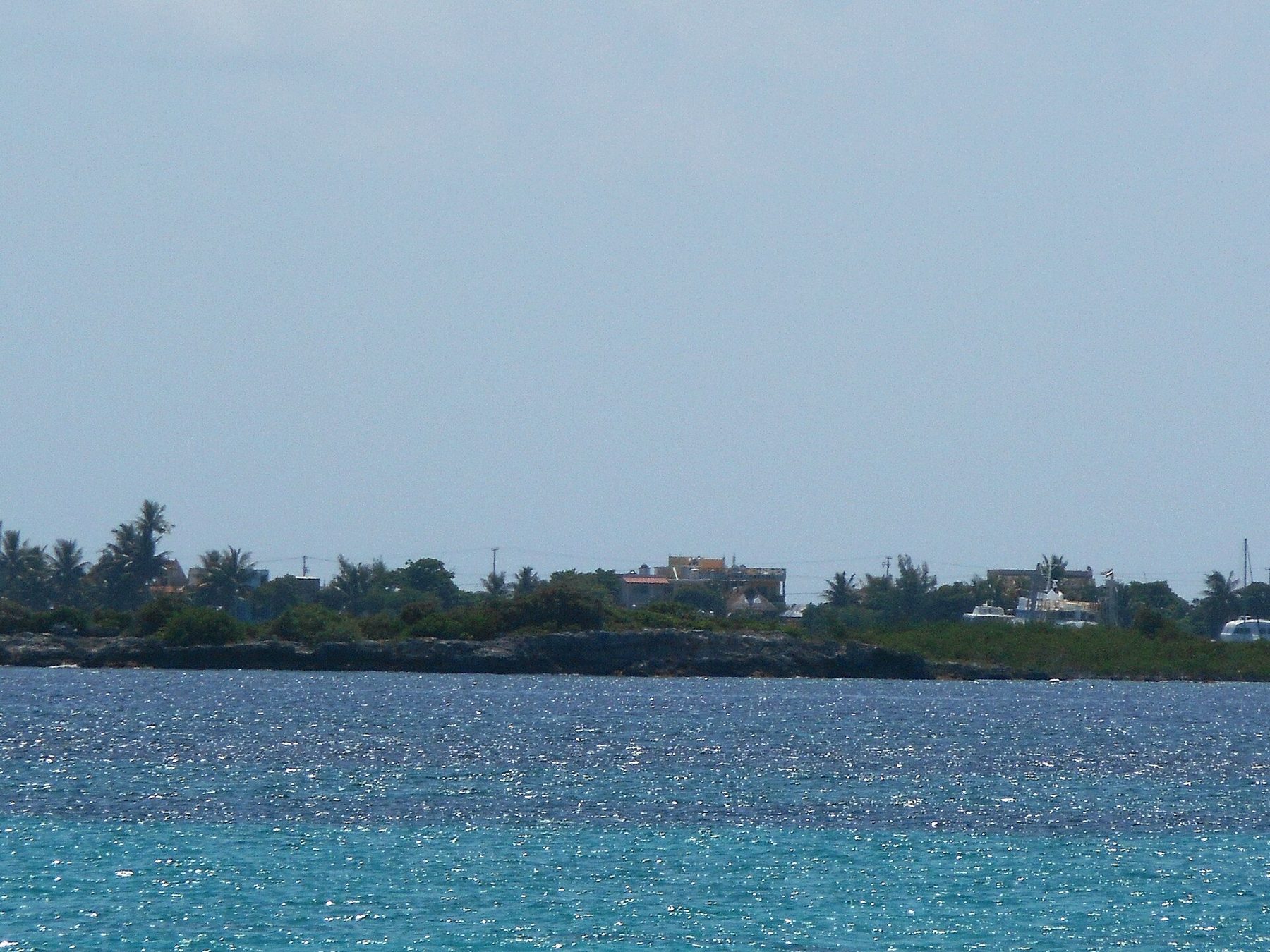 Isla Mujeres seen low on the horizon across open blue water from the deck of a passenger ferry