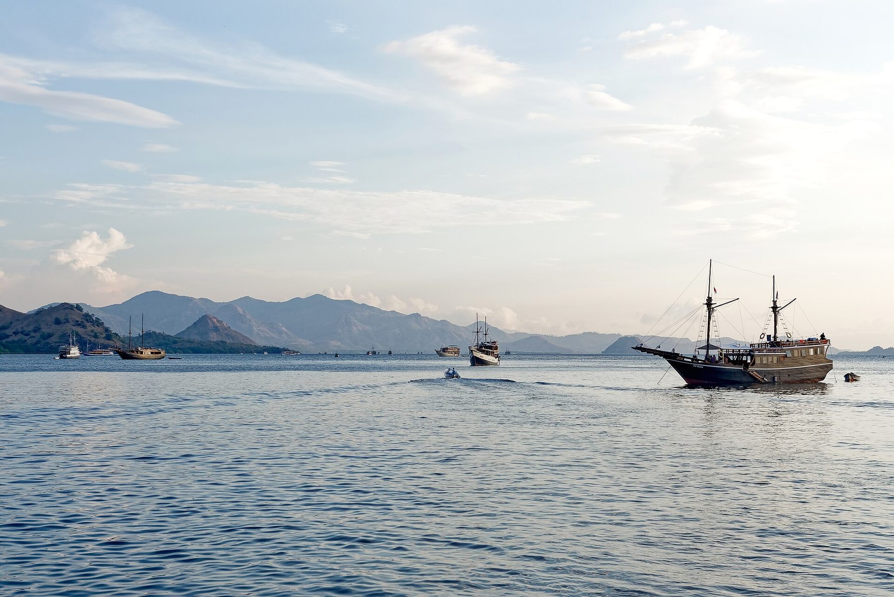 Two small boats crossing choppy open water between dry green islands near Kelor Island