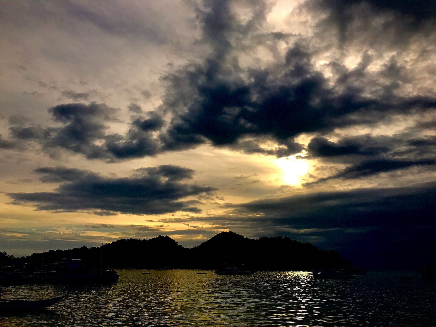 Dusk over Labuan Bajo, with orange light on the water, moored boats in silhouette and hills darkening behind the bay