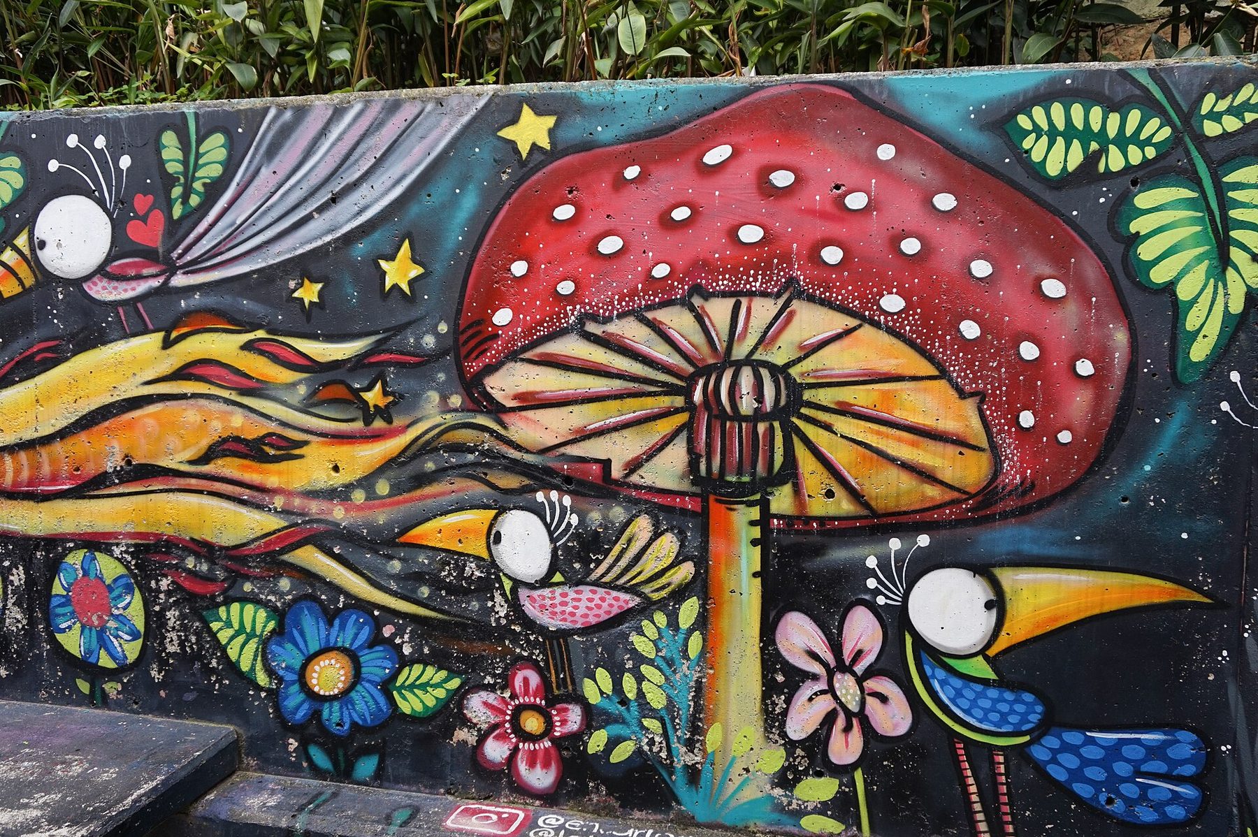A large painted mural in blues, oranges and greens covering a concrete wall beside a stairway in Comuna 13, San Javier, Medellín