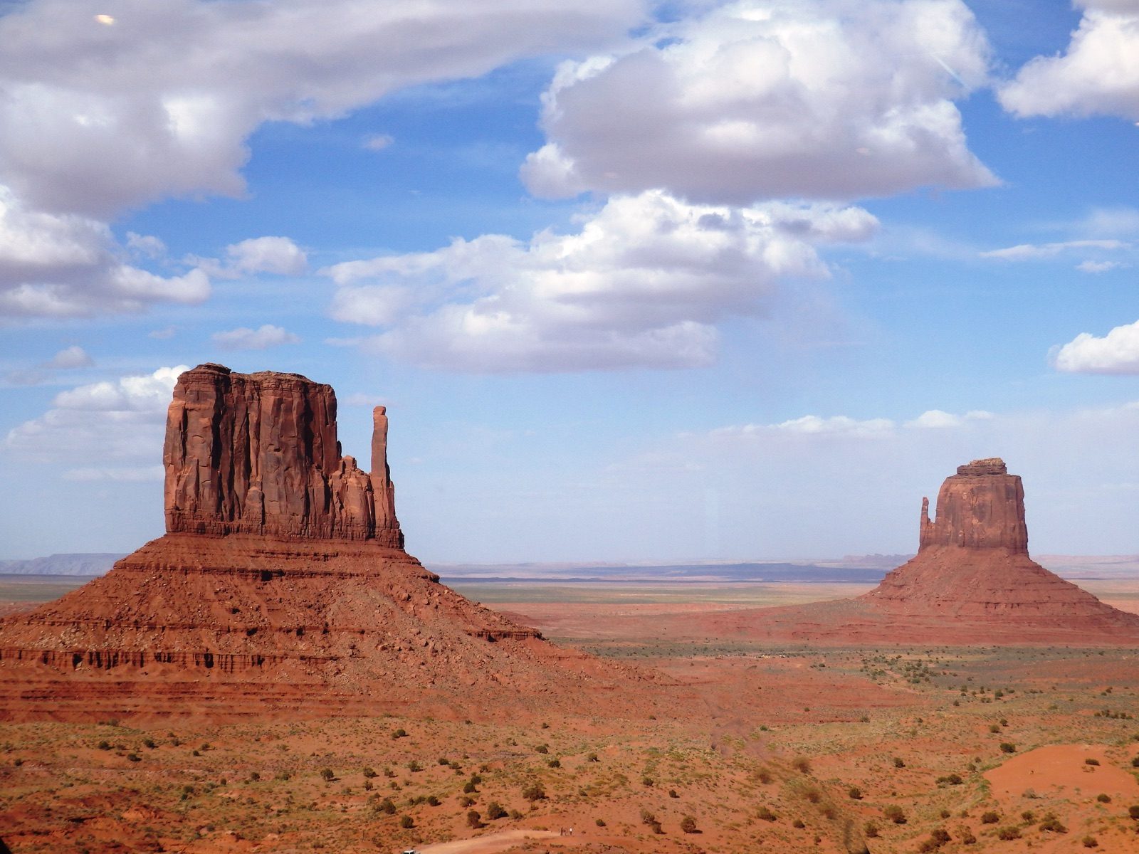 The East and West Mitten buttes rise from the red desert floor of Monument Valley under a clear sky