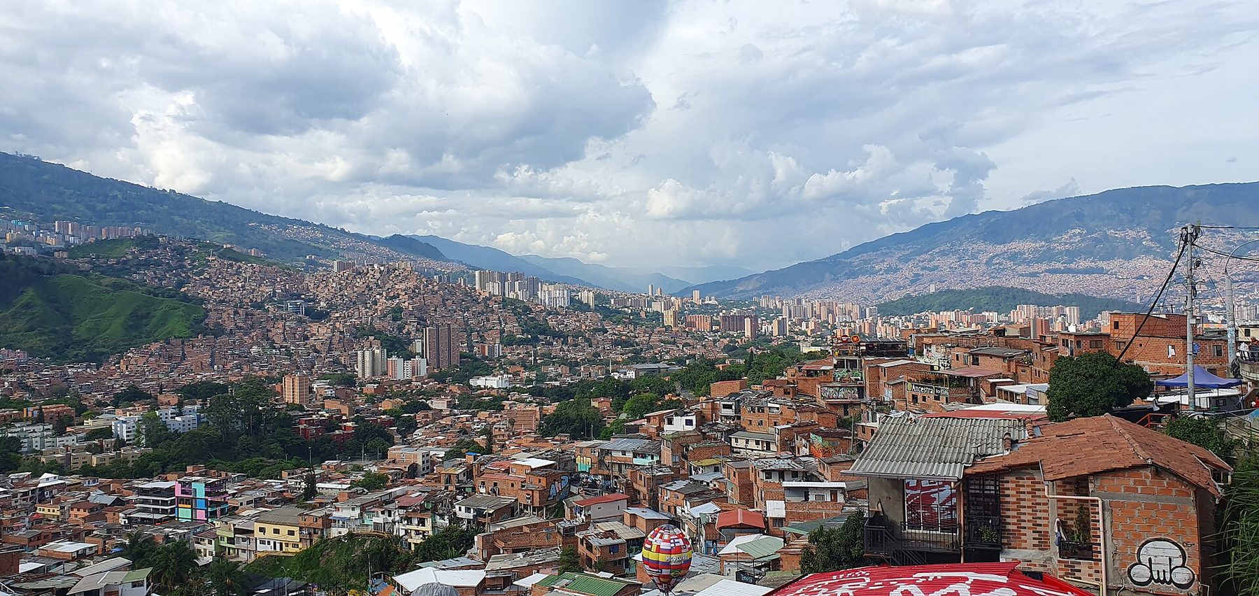 A painted concrete pathway runs between close-set houses in Comuna 13, murals on the walls and hills in the distance