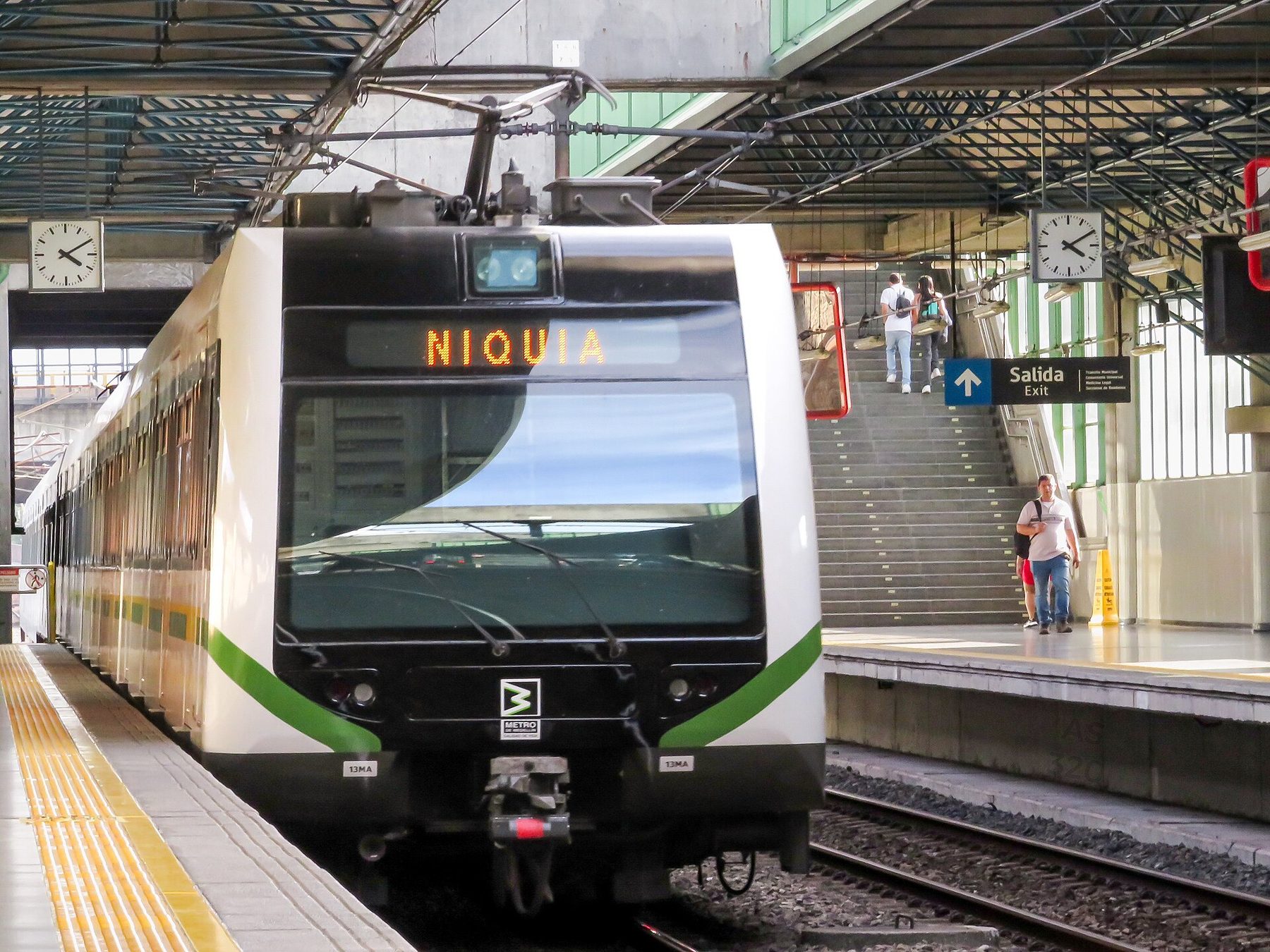 A modernized Medellín Metro train pulls into the open platform at Estación Caribe, with the station canopy overhead