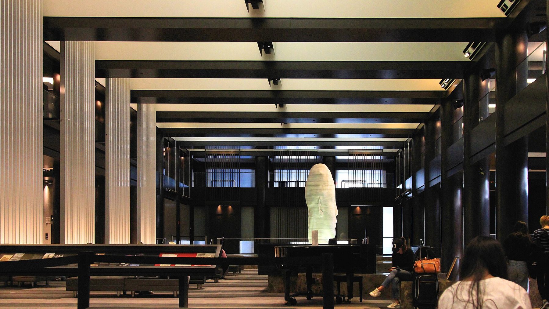 A hotel lobby with dark wood paneling, a patterned carpet, low armchairs and a bar at the far end