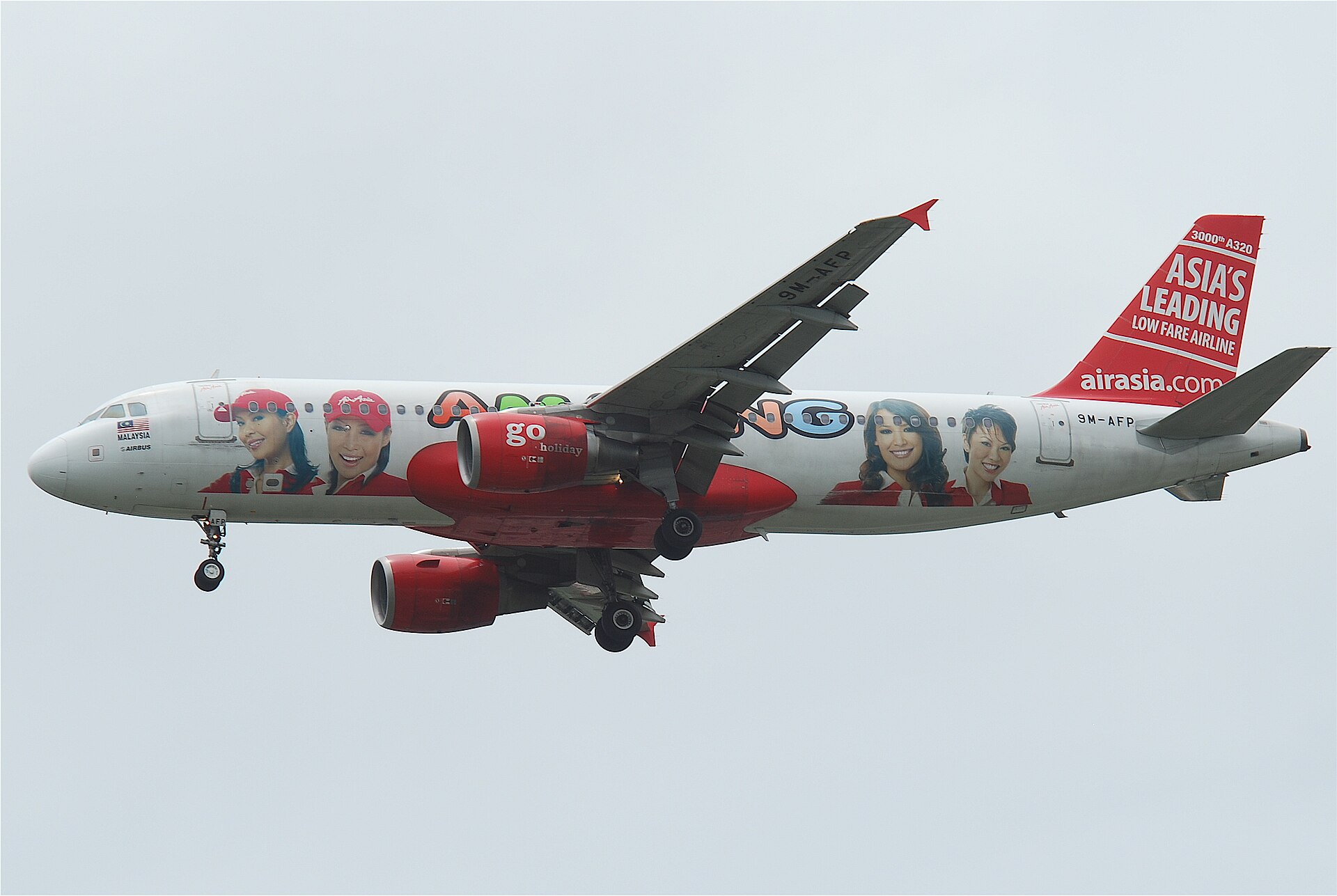 A red and white AirAsia Airbus A320 in a promotional livery, landing gear down, against an overcast sky