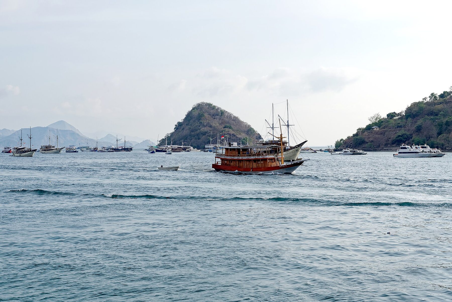 Dive and passenger boats moored in a calm harbor below dry green hills at Labuan Bajo