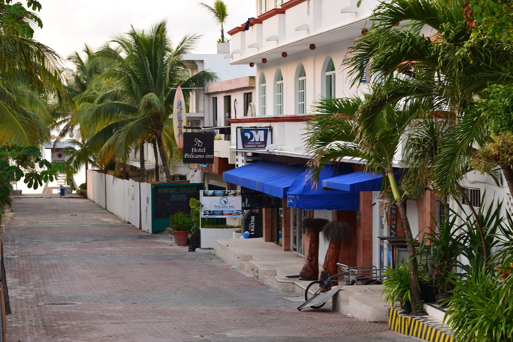 A quiet downtown Playa del Carmen street of low buildings, shopfronts and parked cars under a bright sky