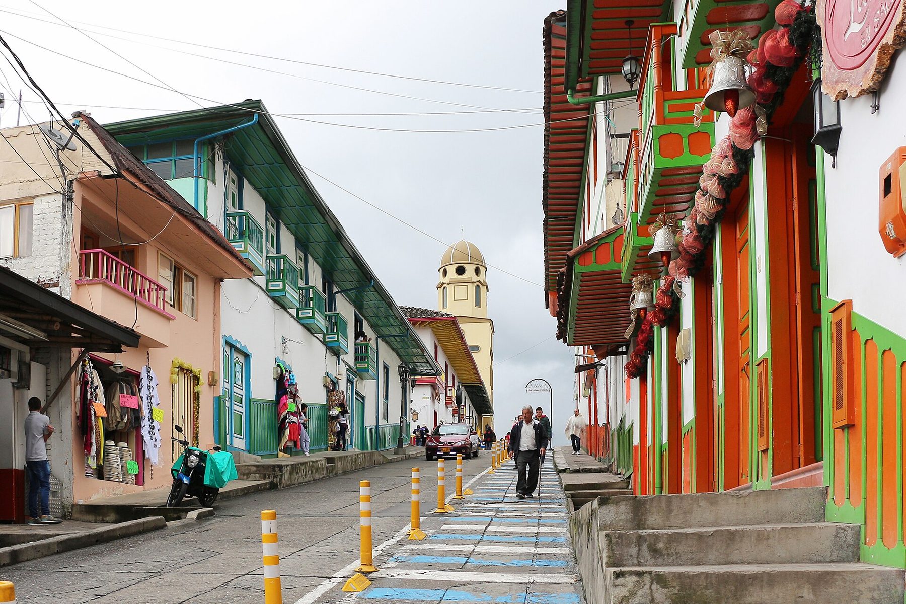A narrow street of low, brightly painted houses with wooden balconies and shopfronts running downhill in Salento.