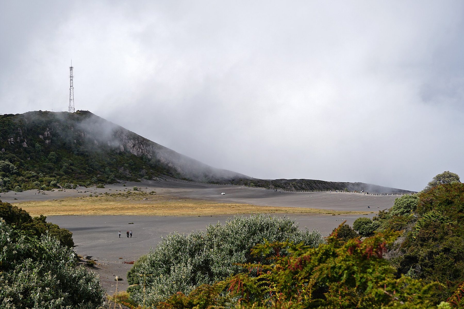 A broad grey volcanic crater with steep eroded walls and a flat sandy floor under a bright sky