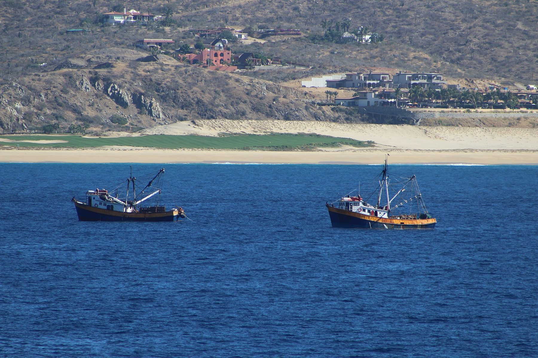 Boats at anchor on calm water at Cabo San Lucas, with the dry brown hills of Baja California Sur behind them