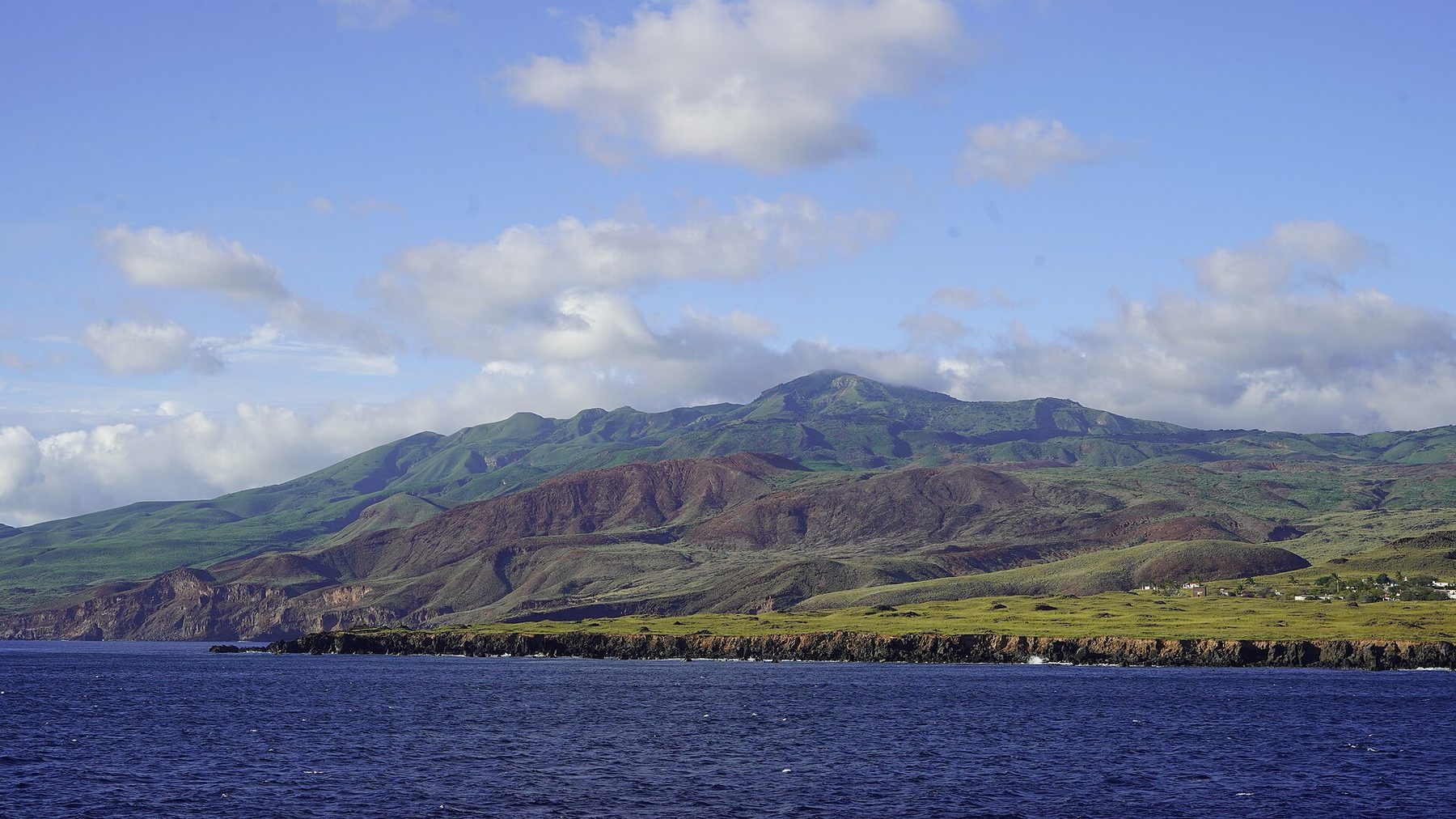 A volcanic island rising out of the Pacific, dark lava slopes under low cloud, with no buildings in sight