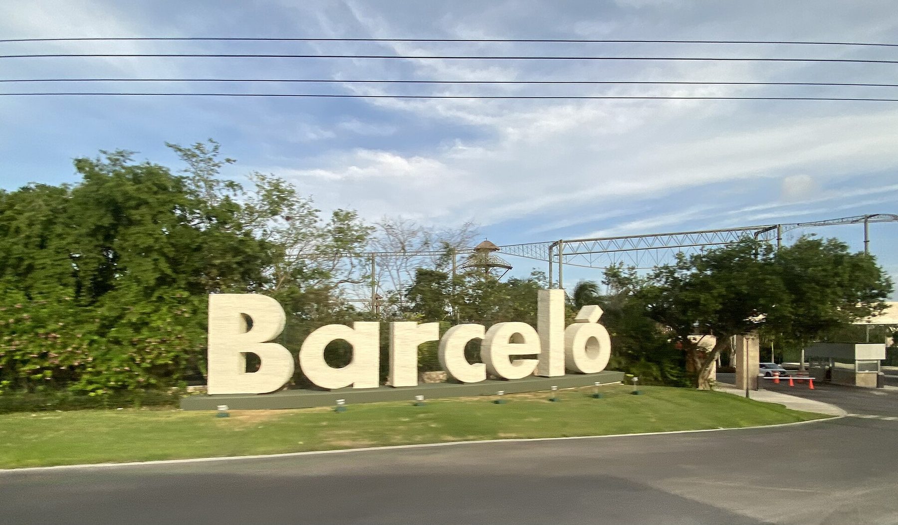 A blue roadside sign for a Riviera Maya resort beside the divided lanes of Highway 307, with low jungle on both sides