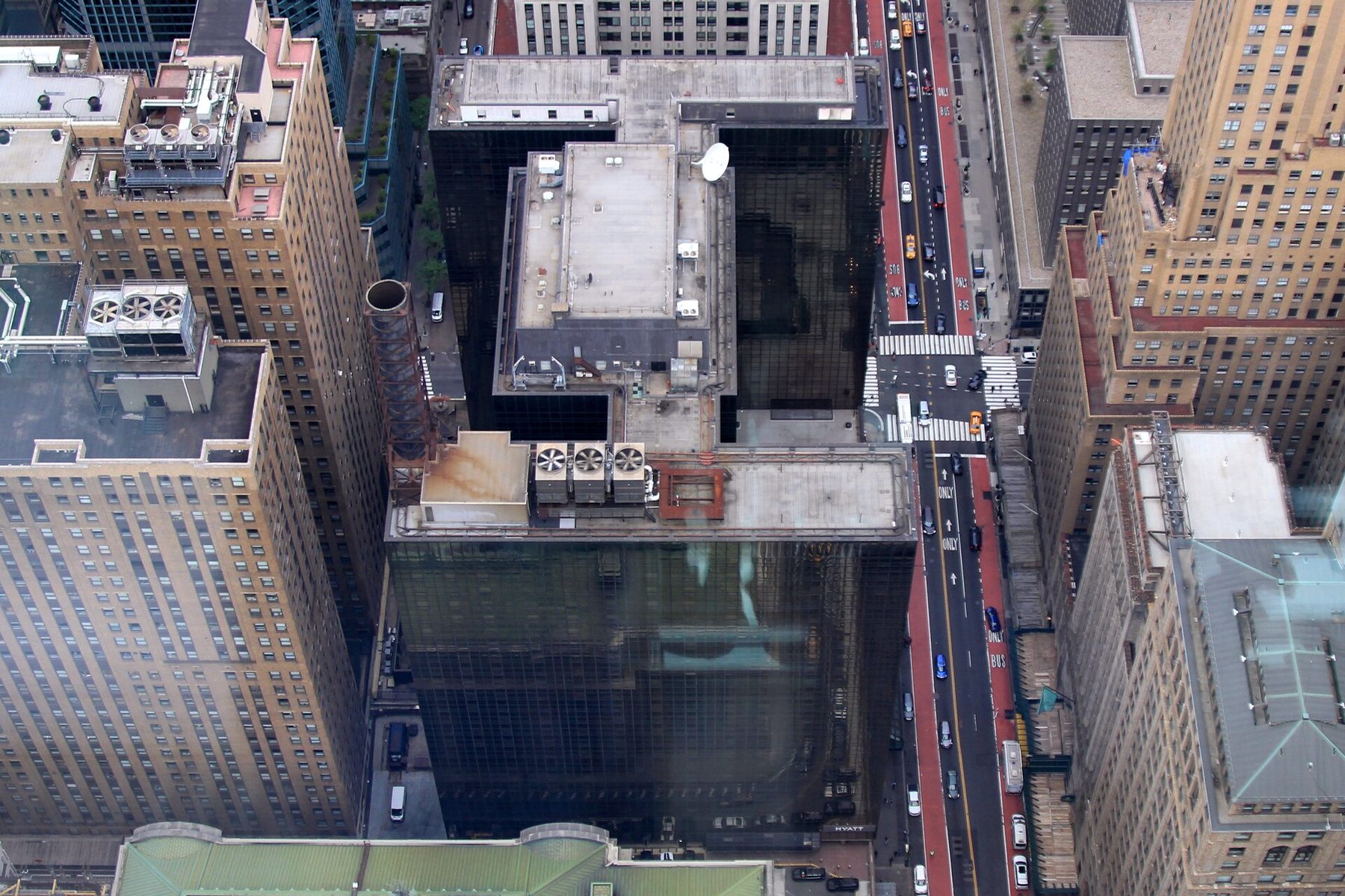 A tall dark glass hotel tower seen from above among the rooftops of Midtown Manhattan