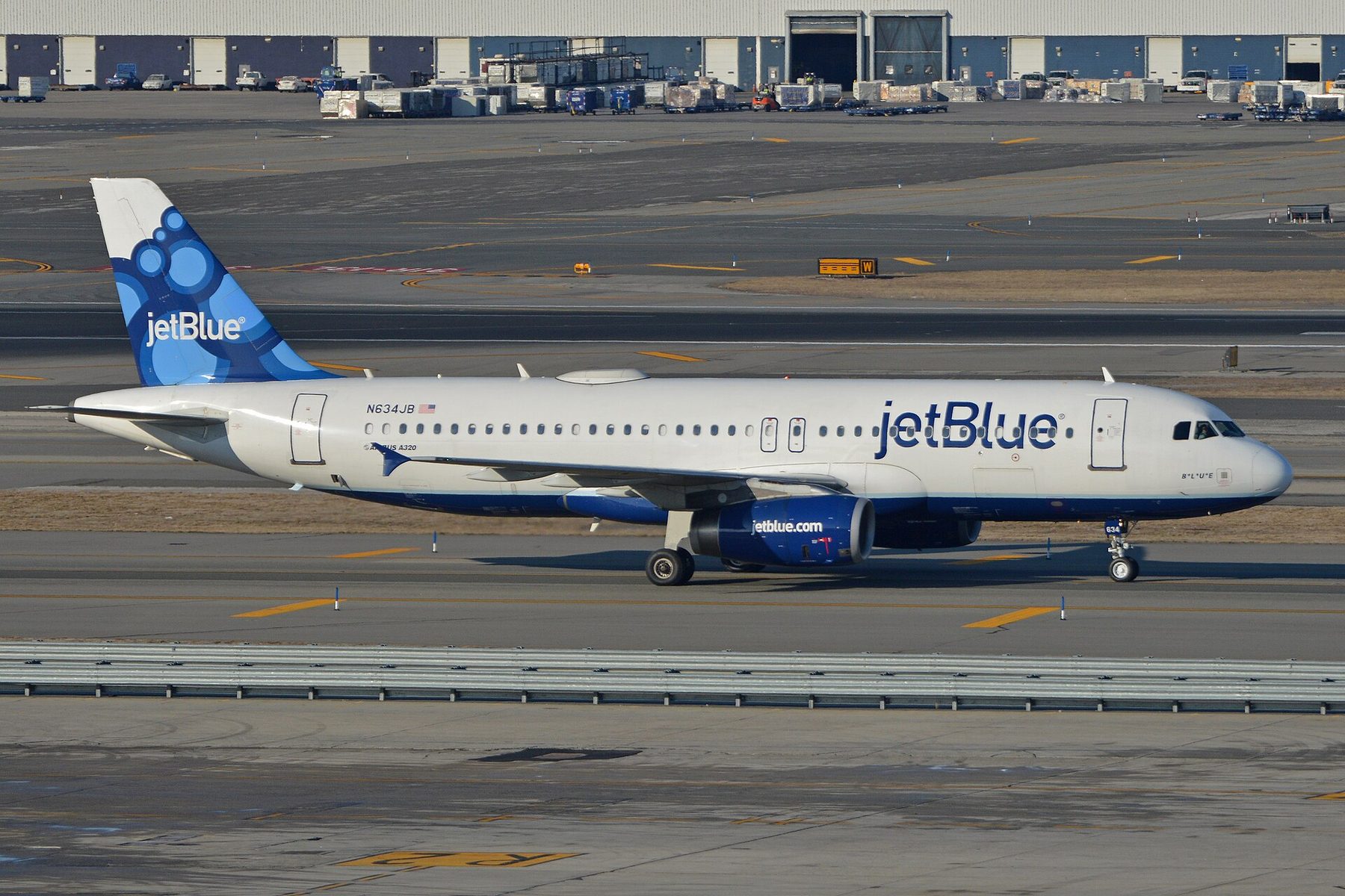 A JetBlue Airbus A320 in white and blue livery taxis on the apron at an airport
