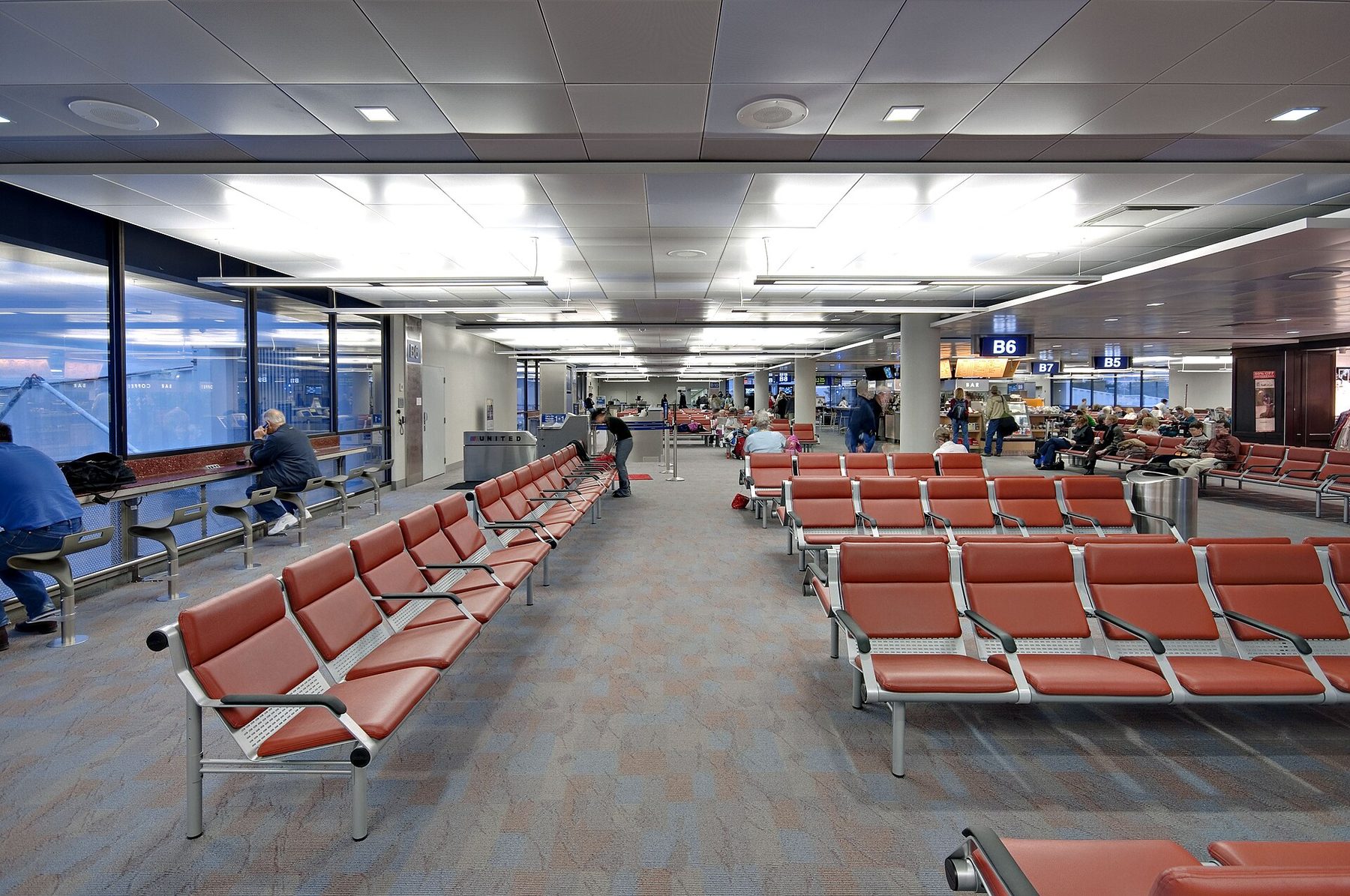 Rows of orange seats at gates B5 to B7 at Tucson International Airport, travellers waiting and a United counter at the back