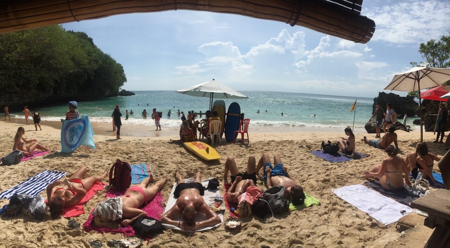 A narrow beach between tall limestone cliffs, with surf running in over a reef and a rock arch at one end