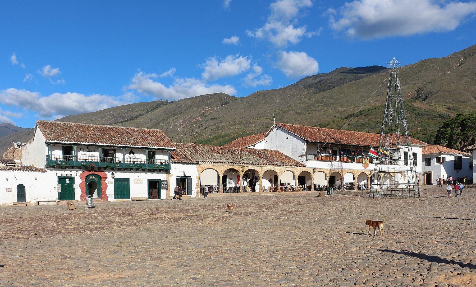 A vast cobbled square edged by low whitewashed buildings with wooden balconies, a white church at one end and green hills behind