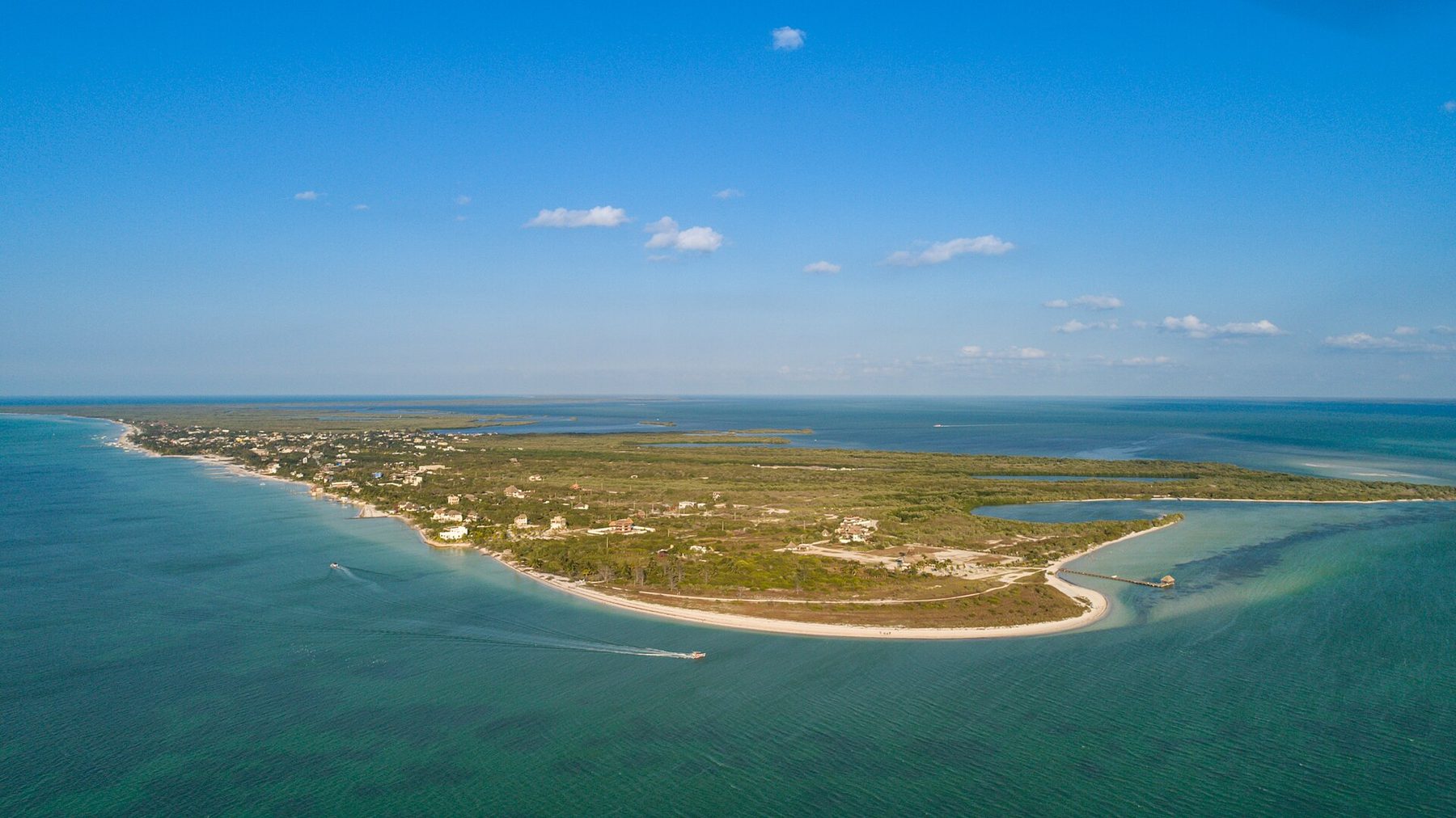 An aerial view of Isla Holbox, a long low sandbar island with shallow turquoise water, pale beaches and green scrub