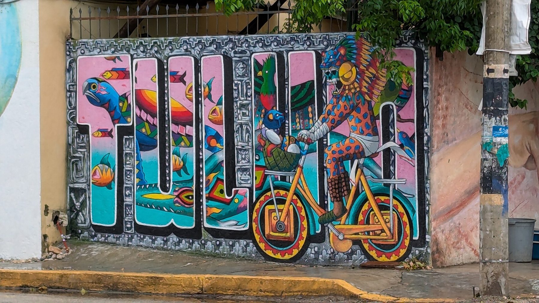 A painted mural of large block letters on a wall in Tulum town with a bicycle leaning against it on the pavement