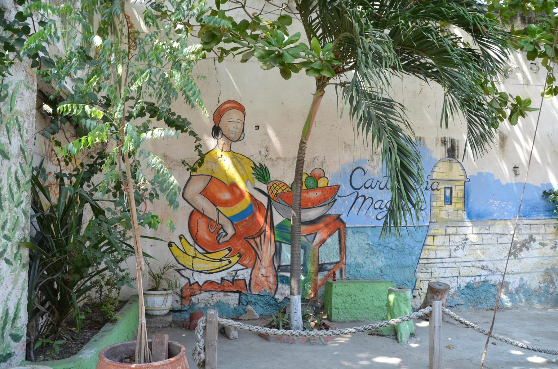 A painted mural of a face in blues and ochres covering the wall of a low house on a narrow Getsemaní street, with a wooden door and a hanging plant
