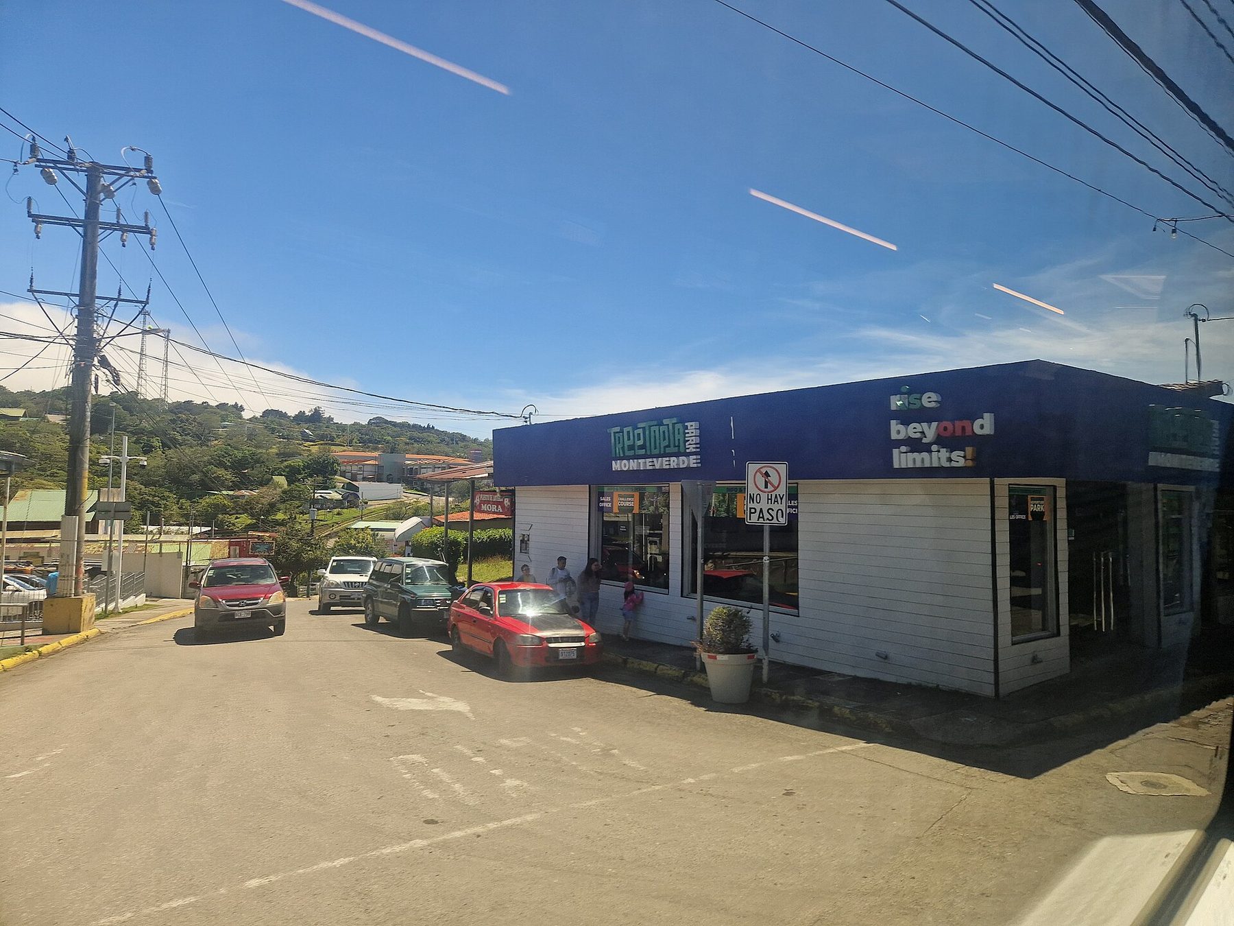 A street in Santa Elena lined with low shopfronts and parked pickup trucks, green hills rising behind the rooftops