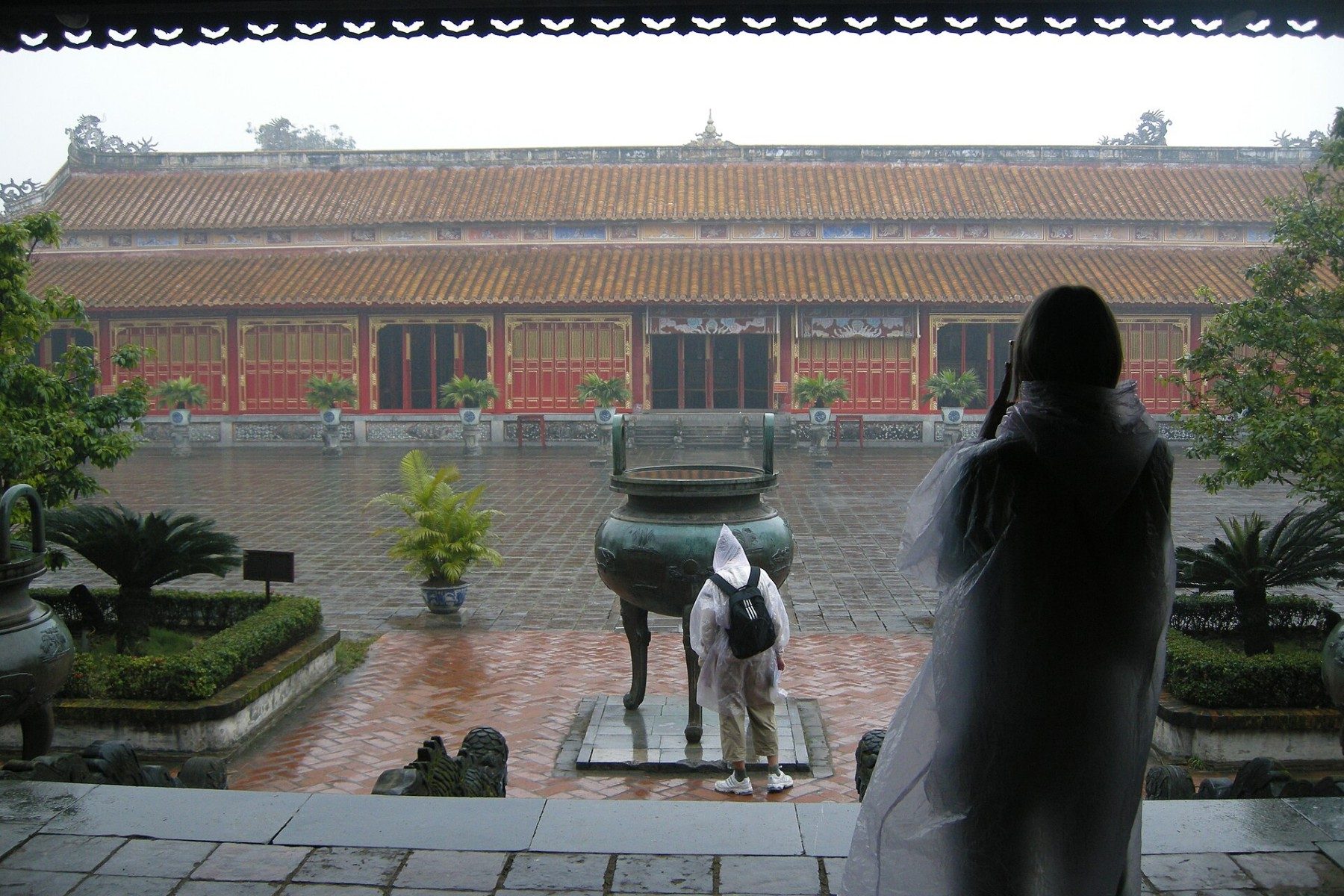 Visitors in rain ponchos cross a wet courtyard in front of a temple at The Mieu.