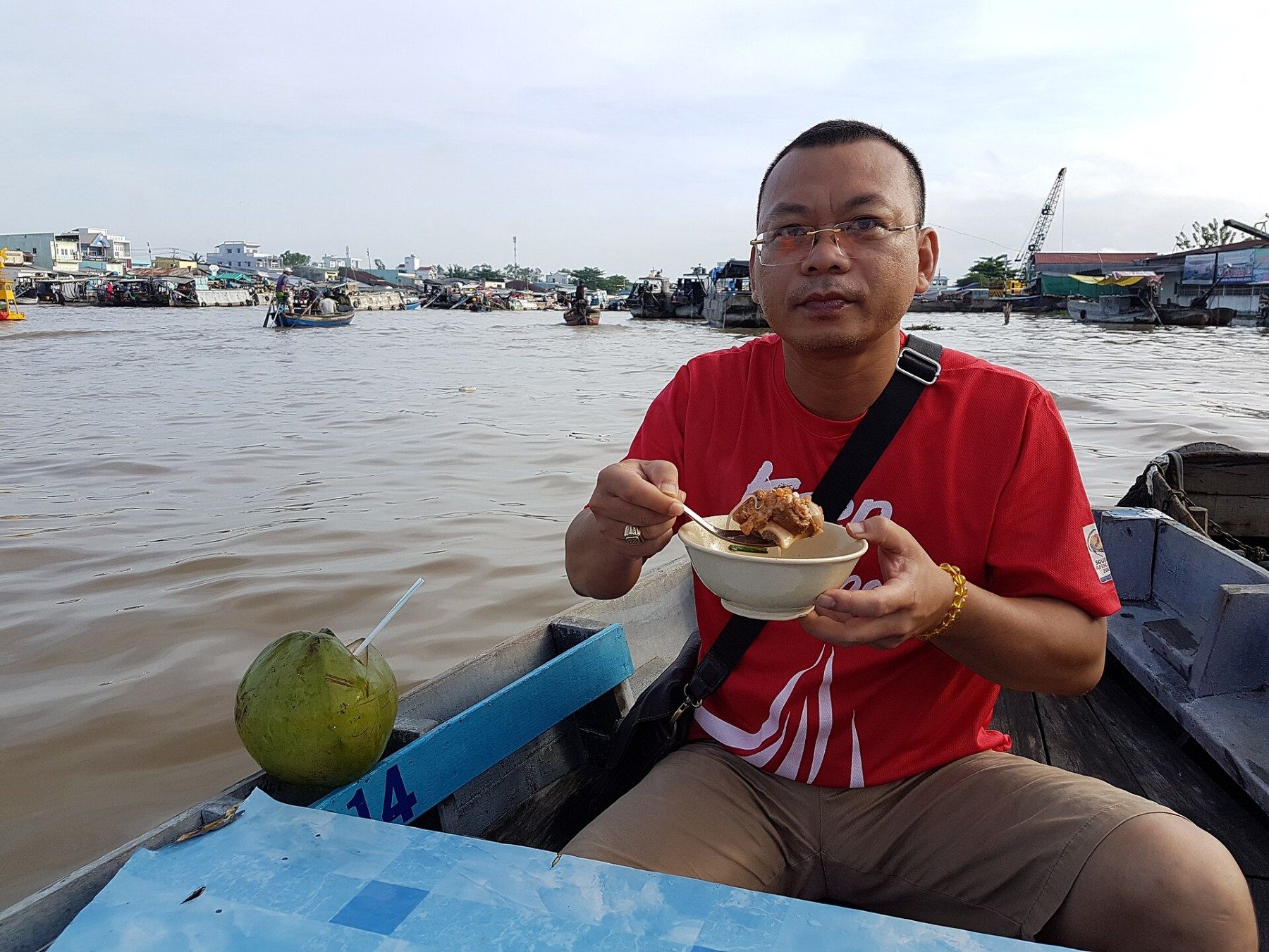 A person eats from a bowl on a boat at Cai Rang floating market.